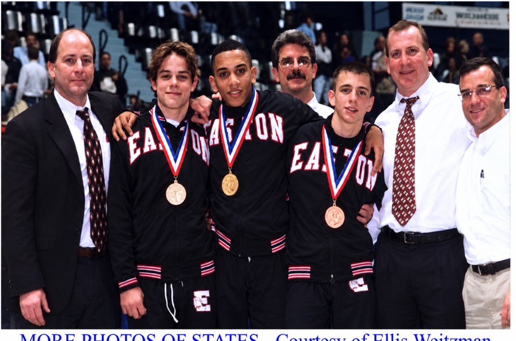 Three Easton wrestlers wearing state tournament medals with four coaches in a gymnasium.